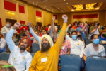 people in turbans cheer and put fists in the air in front row of crowd at conference