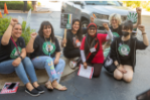 group of Starbucks workers in SWU T-shirts sits on sidewalk at conference, smiling at camera