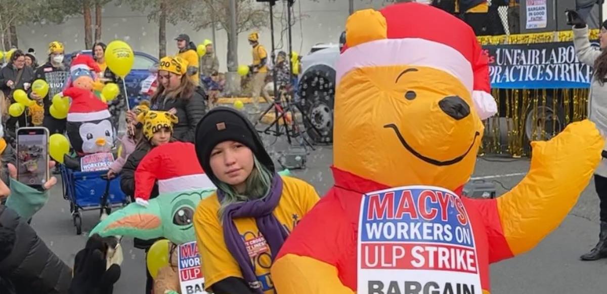 A line of children and adults push baby carriages with inflatable animals wearing signs saying ‘Macy’s Workers on ULP Strike’