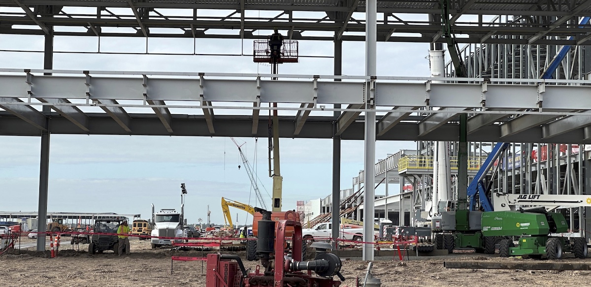 The skeleton of a giant building with a worker in a manlift is shown.