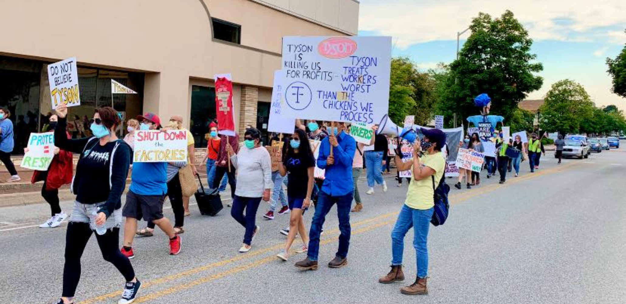 Masked people march with signs: "Tyson Is Killing Us for Profits. Tyson Treats the Workers Worst than the Chickens We Process." "Don't Believe Tyson." "Shut Down the Factories." "Protect = Respect."