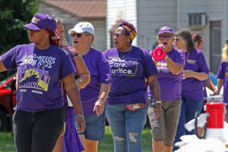 A group of black and white workers wearing purple SEIU T-shirts march.