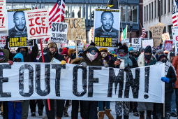 A big crowd carries a banner “ICE out of MN!”