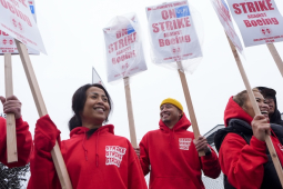 Five women and men in red hoodies that say “strike strike strike” hold picket signs