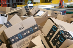A pile of Amazon boxes is shown with workers small in the background