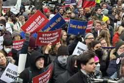 A sea of faces in a protest crowd. Some printed signs say "Stop the Billionaire Takeover," "Hands Off Workers Data," "Stand, Unite, Fight," and "Nobody Elected Musk." Some handlettered signs say "Congress, WYA?" and "He doesn't even go here!"