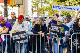 a line of retirees protest behind a metal barrier