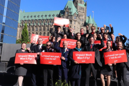 20 flight attendants in uniform hold red signs saying “unpaid work won’t fly” in both French and English 