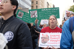 Several workers with signs march towards the camera.  Some say “Hands Off” our workers, our union, Social Security and other items