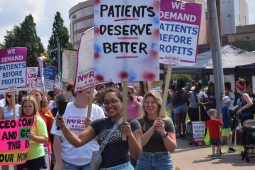 A group of nurses hold picket signs by a street
