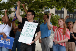 Several people raise their fists, one holds a homemade sign saying “support EPA dissent”