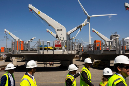 A group of people in hi-viz vests and hardhats walk by huge turbine components