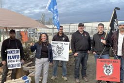 A group of people hold picket signs in front of a canopy.