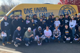 Thirty people pose with a yellow van behind them that says One Union, One Family