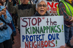 A woman holds a sign at a rally that reads Stop the Kidnappings! Protect Our Neighbors!