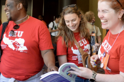Two women and a man, all wearing Somerville Educators red T-shirts, laugh as they look at a book
