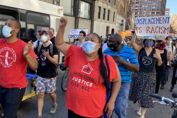 Marchers wearing masks walk through the streets of New York City, with Jabari Brisport and Marcela Mitaynes in the front.