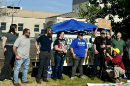 Ten people, some with Machinists Union shirts, stand with a Machinists Local 160 banner