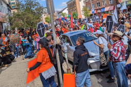 A crowd fills the street holding signs, some of them shaped like coffins.