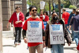 Workers in red shirts march outside the Washington Post's office, carrying signs with slogans including "Flexible RTO" (which stands for return to office) and Washington Post Tech Guild Unite!