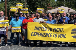A large group stands behind a yellow banner saying “United to Fight, Experience to Win”