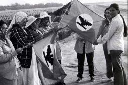 Seven women stand by a car holding a Farmworkers Union flag