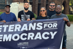 A group of veterans stand behind a blue banner that reads Veterans for Democracy.