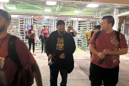 A group of smiling workers leave through factory turnstiles, walking towards the camera.