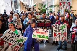 A group of forty cram into a building lobby with signs saying “Labor for Palestine”