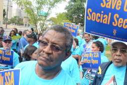 A crowd dressed in light blue T-shirts holds signs saying Save our Social Security and Keep My SSA Office Open.