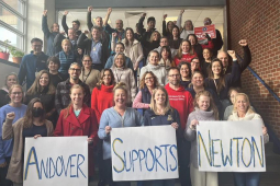 Two dozen teachers stand on stairs with signs saying ‘Andover Supports Newton’