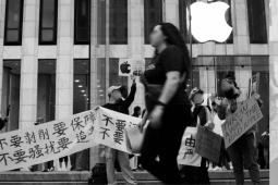 People march in front of an Apple store in New York City, holding signs and banners in English and Chinese. Their faces are blurred out in the photo due to fears of retaliation from the Chinese government against them and their families.