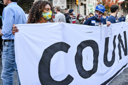 A group of people holds a large white banner with the slogan Count Every Vote.
