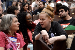 Two women talk across seats in filled auditorium.