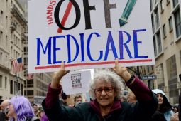 A woman in a big crowd holds up a sign saying ‘hands off Medicare’