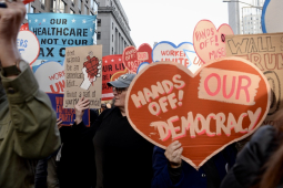 A heart-shaped sign saying “Hands Off Our Democracy” is carried in a crowd.