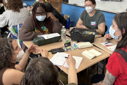 A group of masked people sit around a table discussing something intensely.