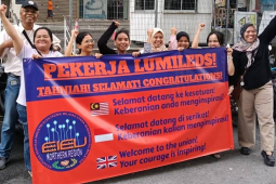 A group of supporters stand behind a red and blue banner congratulating the Lumileds workers on voting for the union and saluting their courage.