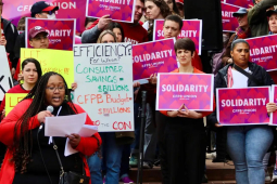 CFPB workers at a rally holding pink signs that say Solidarity and other handmade signs with slogans like CFPB Protects All Consumers.
