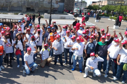 A group of fifty workers red hats and white shirts raise their fists and pose for the camera