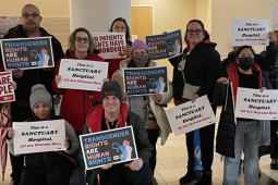 A group of 10 people inside hold signs saying “Nurses Care for All People” and “transgender rights are human rights” 