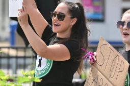 Two young women in Starbucks Workers United T-shirts stand outdoors, holding up cardboard signs, mouths open to yell or chant.