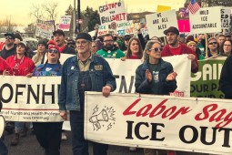 People march in the street carrying various banners and signs. The most visible banners says "Labor says ICE out." Others partially visible are for two Oregon health care unions, OFNHP and ONA. Their red and green shirts (respectively) are also visible, and someone has a blue AFT shirt. Many handmade picket signs are visible, including "We are all Alex," "Unions want ICE out," "Hold ICE accountable," and "Ge(stop)o the bullshit" 