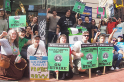 Youngish workers pose with raised fists on a city street. Printed green signs say "OPEIU Local 153, Kickstarter United, On strike," One handwritten sign says "Protect the 4DWW"