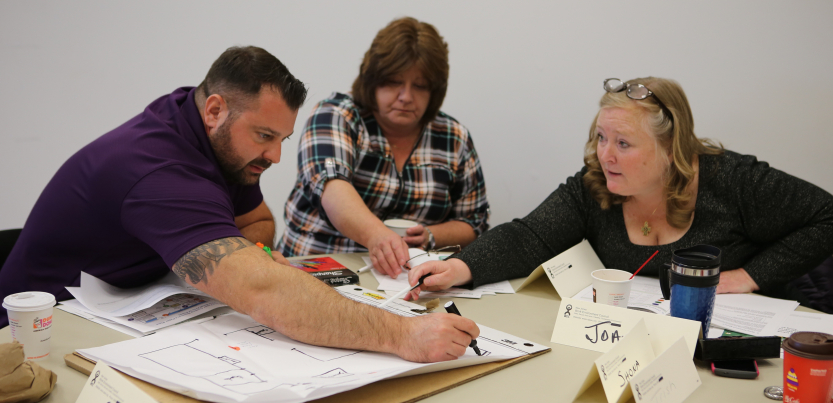 Three workers seated around a table collaborate to draw a hazard map
