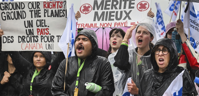 Six picketers hold signs in the rain, including, “Ground our rights? Ground the planes!”