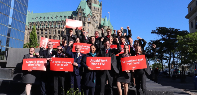 20 flight attendants in uniform hold red signs saying “unpaid work won’t fly” in both French and English 