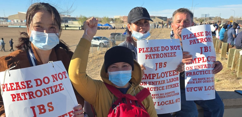 Four strikers holding signs, one with a fist in the air, face the camera.