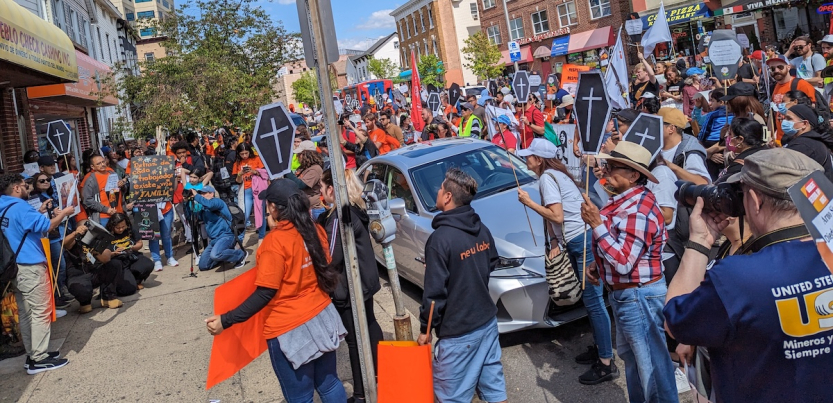 A crowd fills the street holding signs, some of them shaped like coffins.