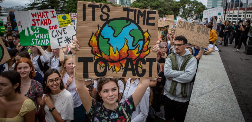 New Zealand students hold signs with slogans like "It's Time to Act," with a drawing of the earth being consumed by flames, during a school strike in March 2019.